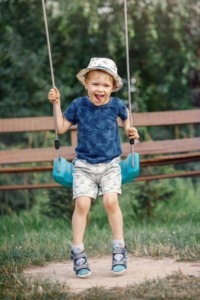 One cute little boy having fun on a swing in beautiful summer garden on warm and sunny day outdoors. Active summer leisure for kids. stock photo