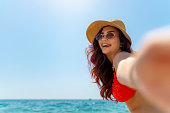 Smiling girl in straw hat and sunglasses take a selfie at the beach.