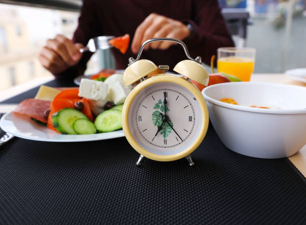 istock Close up  yellow alarm clock while man Intermittent fasting concept with eating salad  plates. Time to lose weight , eating control or time to diet concept 1394760059