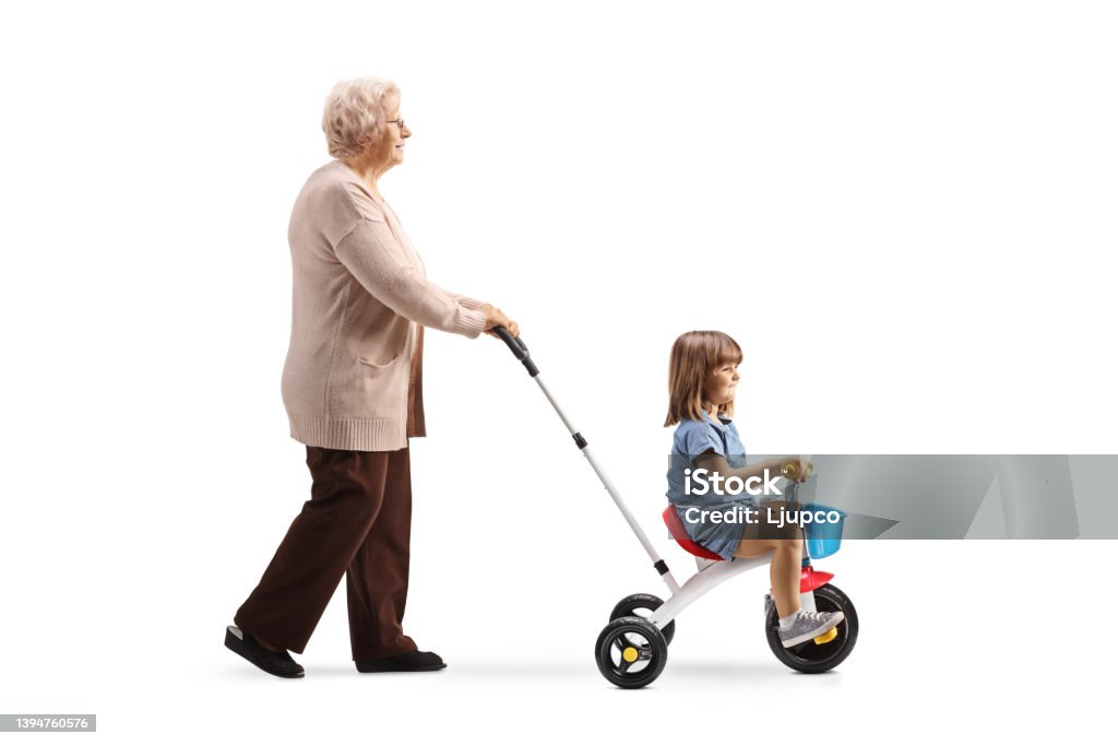 Full length profile shot of a grandmother pushing a girl on a tricycle Full length profile shot of a grandmother pushing a girl on a tricycle isolated on white background 2-3 Years Stock Photo