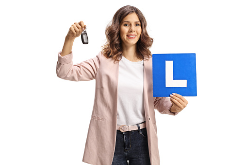 Young woman holding car keys and a learner plate for drivers isolated on white background