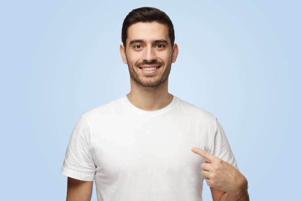 istock Smiling attractive nice man points at his blank white t-shirt with index finger 1394760869