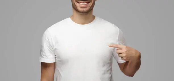 Photo of Young man pointing with index finger at blank white t-shirt with empty space