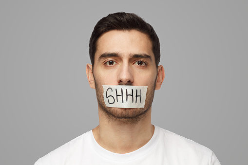 Close up shot of young man with taped mouth with shhh text on it