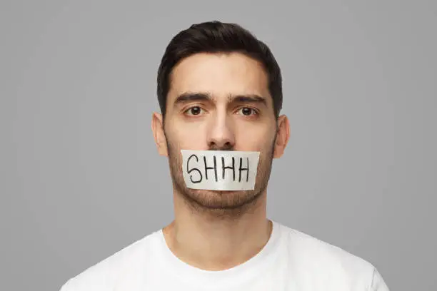 Photo of Young man with taped mouth with shhh text on it