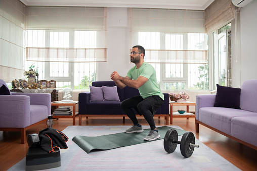 Young man doing sports at home to live healthy. desk worker man doing sports at home. Man doing sports to look fit in summer. Young man in glasses training to have a fit body at home with a gym mat and some small gym equipment.