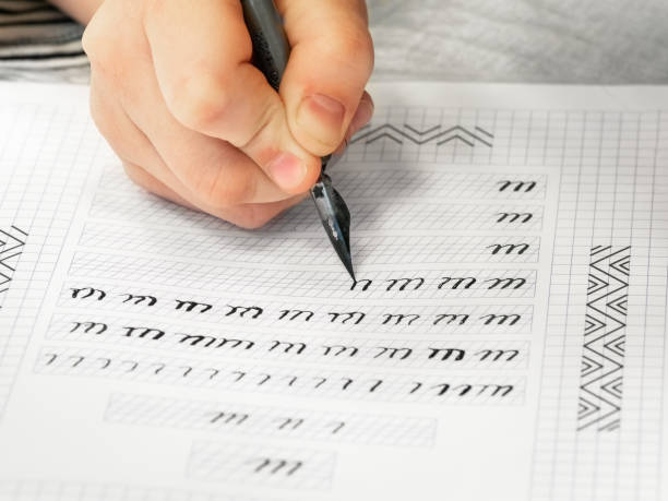 istock Close-up pupil's hands are writing calligraphy in a notebook. Schoolboy calligraphy performs a task at the workplace. Concept of children's education, teaching knowledge, skills and abilities. 1394761872