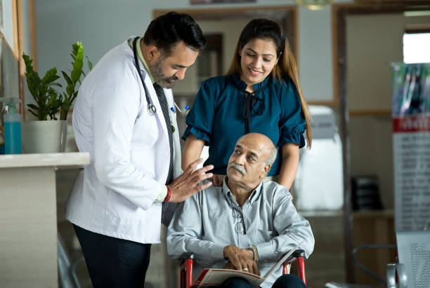 Doctor consoling disabled man on wheelchair with daughter by his side at the hospital Male doctor and disabled old man in wheelchair with daughter by his side at the hospital corridor india hospital stock pictures, royalty-free photos & images