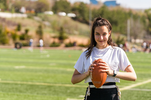Portrait of a young woman holding a football on a field