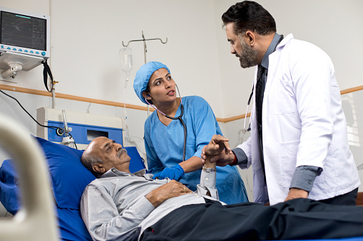 Male doctor with nurse examining old patient lying on hospital bed