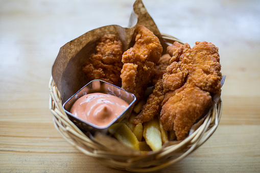 Crispy fried Kentucky chicken wings in a basket, with French fries and sauce.