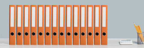 Colorful document binders or lever arch file on a shelf or desk banner A row of mockup orange document binders or lever arch file with paperwork on an office shelf or desk. Calculator and pencils. Business concept banner. Copy space neat office stock pictures, royalty-free photos & images