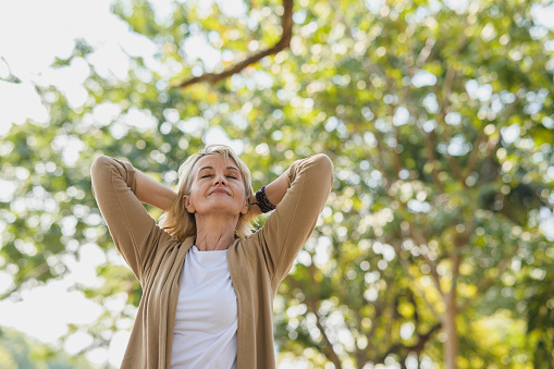 Portrait photo of happy senior Caucasian woman relaxing and breathing fresh air with sunlight in outdoors park. Elderly woman enjoying a day in the park on summer. Healthcare lifestyle and wellness