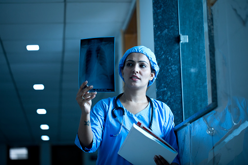Female doctor examining x-ray report at hospital corridor