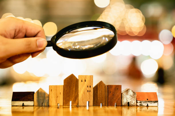 Hand holding magnifying glass and looking at house model, house selection, real estate concept. stock photo