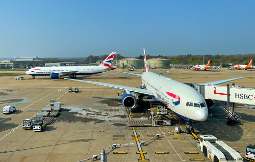 Gatwick, United Kingdom - 25 March 2022:  One plane taxis along the runway past others on stand at Gatwick Airport