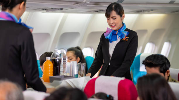 Two young beautiful Asian flight attendant serving food and drink to passengers on airplane. Two stewardess pushing food cart along aisle to serve the customer. Airline service business concept. Two young beautiful Asian flight attendant serving food and drink to passengers on airplane. Two stewardess pushing food cart along aisle to serve the customer. Airline service business concept. airplane food stock pictures, royalty-free photos & images