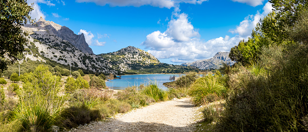Wide panorama photography of the idyllic water reservoir Embassament de Cúber at the foot of Mallorcas highest mountain Puig Major with the hiking trail GR-221 illuminated by sunlight in springtime.