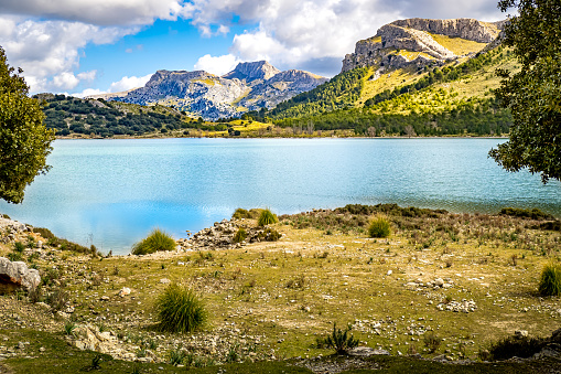 Springtime with sunshine and clouds at the artificial shore of Palma de Mallorcas water reservoir called embassament de cuber with the mountains Morro de Cuber and Serra dels Teixos in the background.