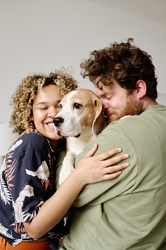 Multiethnic couple embracing their small member of family with love, they happy to have a dog