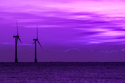 Surreal purple sky at twilight with silhouette of wind turbines on the sea horizon. Beautiful skyscape background image. New age spiritual landscape with a futuristic perspective on climate change.