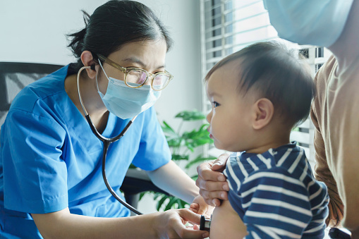 Asian pediatrician or doctor or nurse examining and listening lungs of little baby boy with stethoscope in the medical room.
