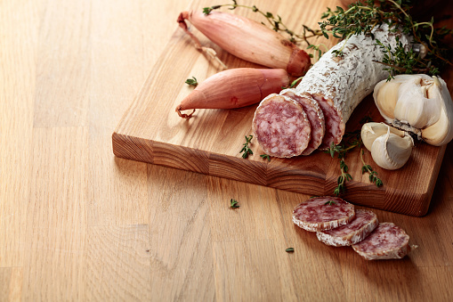 Traditional dry-cured sausage with thyme, garlic, and onion. Dry-cured sausage on a wooden table.
