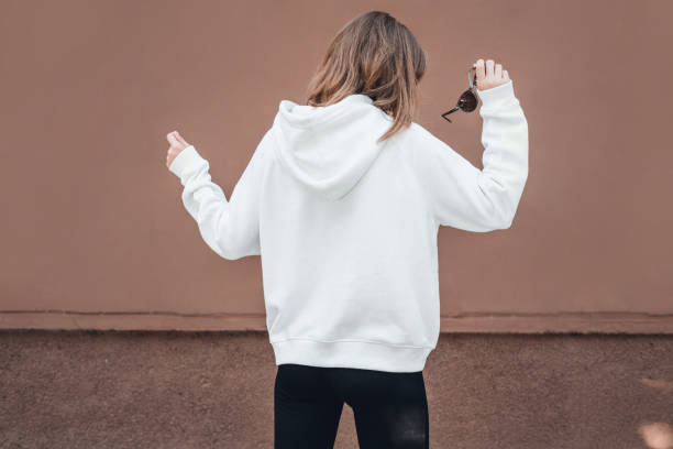 Osoba w białej bluzie odwróciła się, trzymając okulary przeciwsłoneczne i ilustrując wskazówki dotyczące pielęgnacji bluzy.