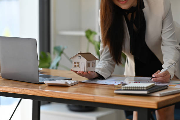 cropped ver jovem asiática em pé no escritório segurando um modelo de casa e trabalhando em uma papelada, para o conceito de imobiliário, negócios, finanças e tecnologia. - approved lease agreement insurance document - fotografias e filmes do acervo