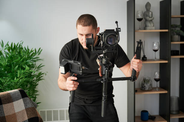 Videographer man with camera mounted on gimbal stabilizer equipment indoors. Videographer man shooting footage indoors, using camera mounted on gimbal stabilizer equipment. camera operator stock pictures, royalty-free photos & images