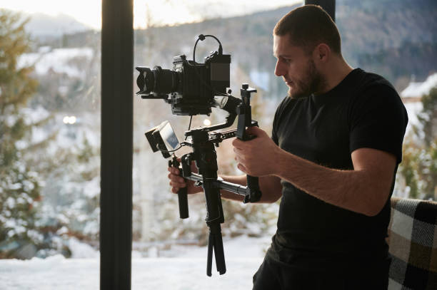 istock Videographer man with camera mounted on gimbal stabilizer equipment indoors. 1394786942