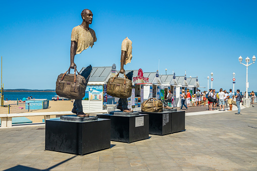 Bronze statues from the exhibition The Travelers by Bruno Catalano exposed on the waterfront of the city of Arcachon, France on a summer day