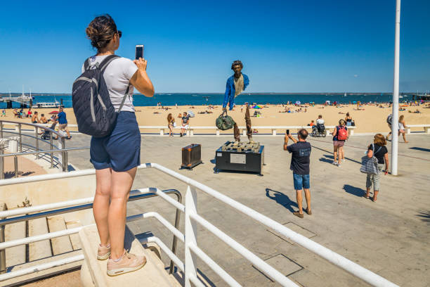 ブルーノ・カタラーノの展覧会「トラベラーズ」からブロンズ像「ブノワ」の写真を撮る女性 - beach body ストックフォトと画像