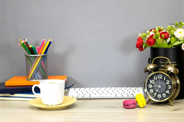 Back to school concept - pencil-box and books, notebook and clock showing seven o'clock and flowers, macaron cookies and keyboard on wooden table