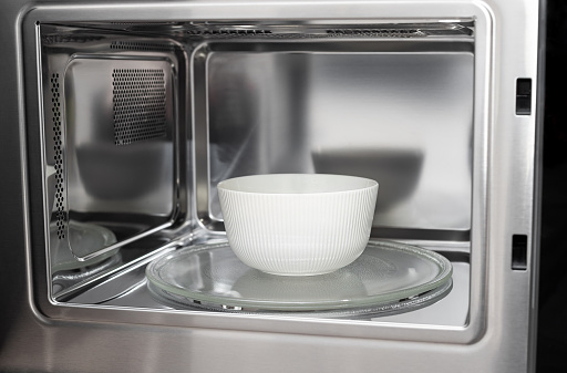 white bowl in modern stainless microwave oven. heating and cooking food. soft focus