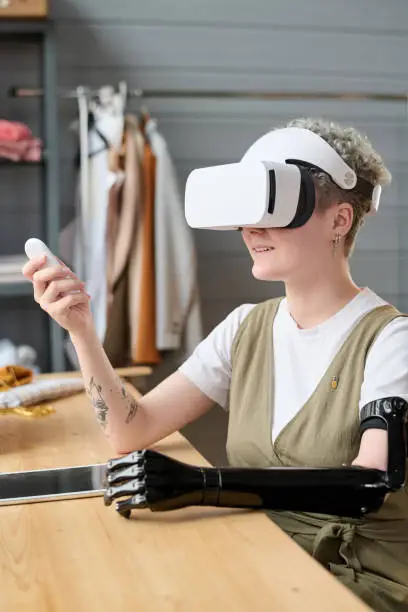 Young modern woman with myoelectric arm in vr headset using remote control while making or preparing presentation of new project