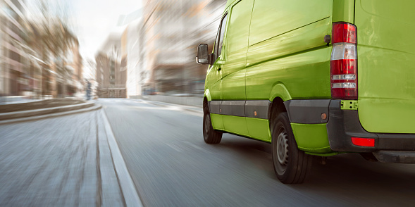 A green delivery van driving on a street in an urban area. Motion blurred background.