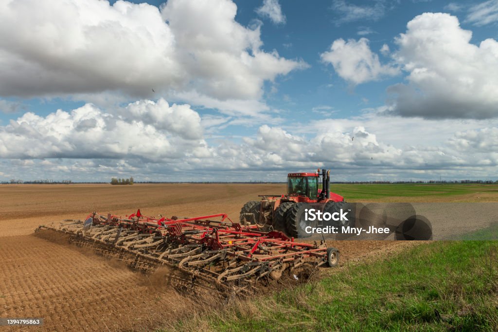 Red tractor cultivates the farm field. Red tractor cultivates the farm field. Spring agricultural works in Ukraine. Plowed soil and sky with clouds. Countryside landscape Plowing Stock Photo