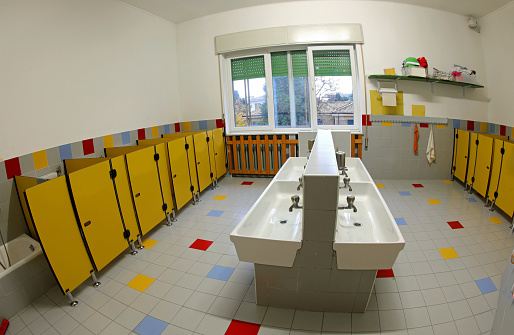 interior of the bathrooms of a nursery school with low sinks and yellow toilet cubicles without children