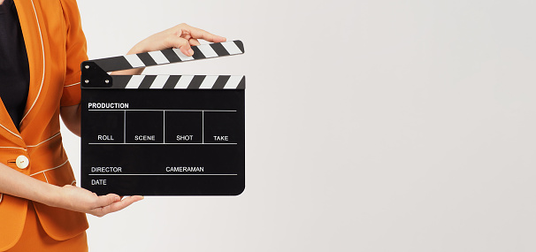 The woman's body part hold a Black Clapperboard or movie Clapper board and she wears a yellow mustard suit on white background.