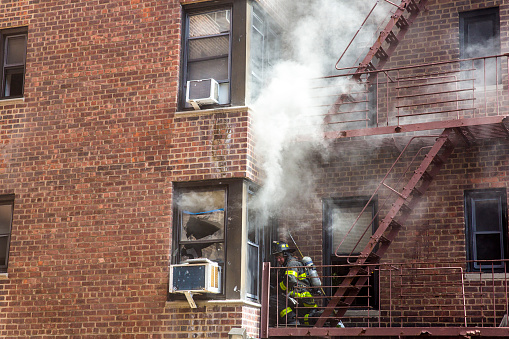 New York city, USA - May 1st 2022:  firefighter is trying to break the window to get in and stop the fire from a burning apartment