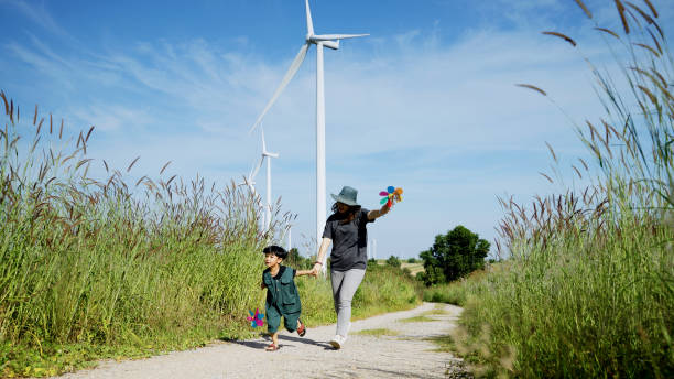 Mother and his son run around with windmills in a wind turbine field, mother teaching his son how to live in harmony with nature and technology, family relationships. stock photo