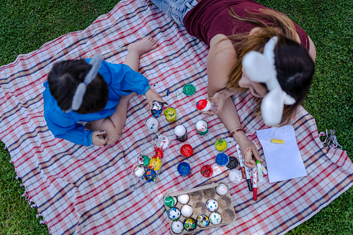 Mother and her baby boy coloring Easter eggs in the garden