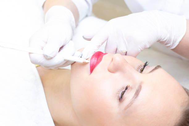 istock Young woman having permanent makeup on her lips at the beauticians salon. Permanent Makeup (Tattoo). drawing a contour with a white lip pencil 1394807020