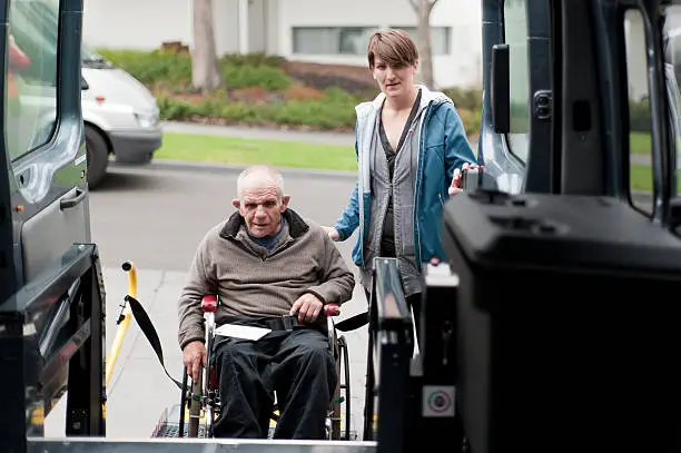 Man in wheelchair entering a modified van shot from inside the vehicle, and with a female support worker by his side.