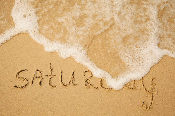 istock Saturday - handwritten on the light beach sand with a soft wave lapping. 1394814493