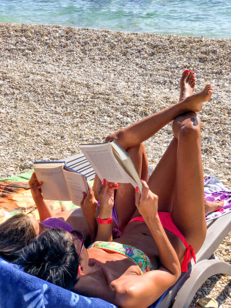istock Mother and daughter enjoying summer vacations while reading a book on the beach 1394814593