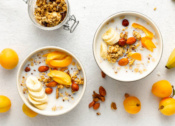 Healthy breakfast cereal top view. Granola breakfast with fruits, nuts, milk and peanut butter in bowl on a white background stock photo