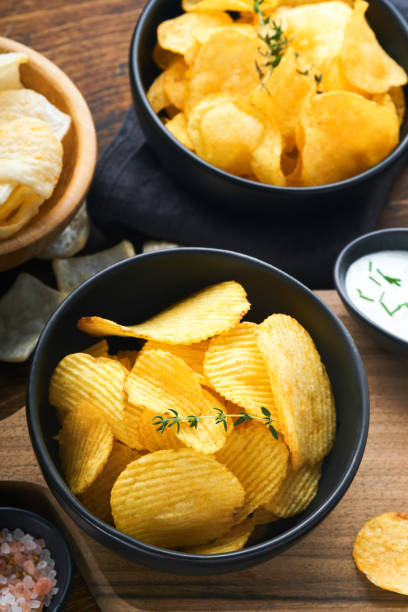 istock Potato corrugatedchips. Fast food. Crispy potato chips ceramic black bowl with sour cream sauce and onions in wooden stand on old kitchen table wooden background. American tradition. Hot BBQ. Top view 1394820587