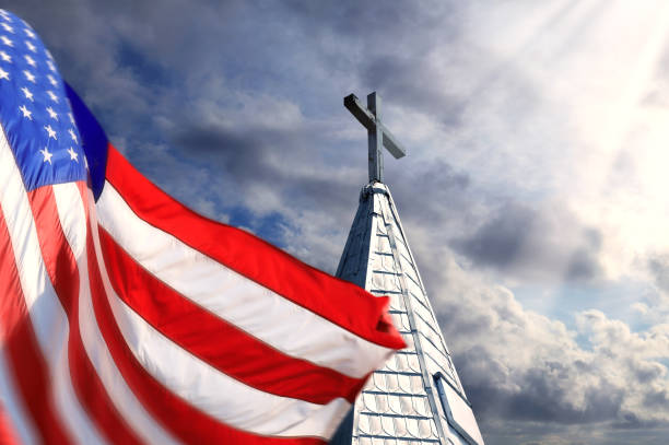 American flag and church rooftop with cross over dramatic sky Close up church and American flag steeple stock pictures, royalty-free photos & images
